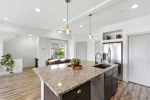 Kitchen with a kitchen island with sink, light stone countertops, stainless steel appliances, pendant lighting, and light wood-style floors