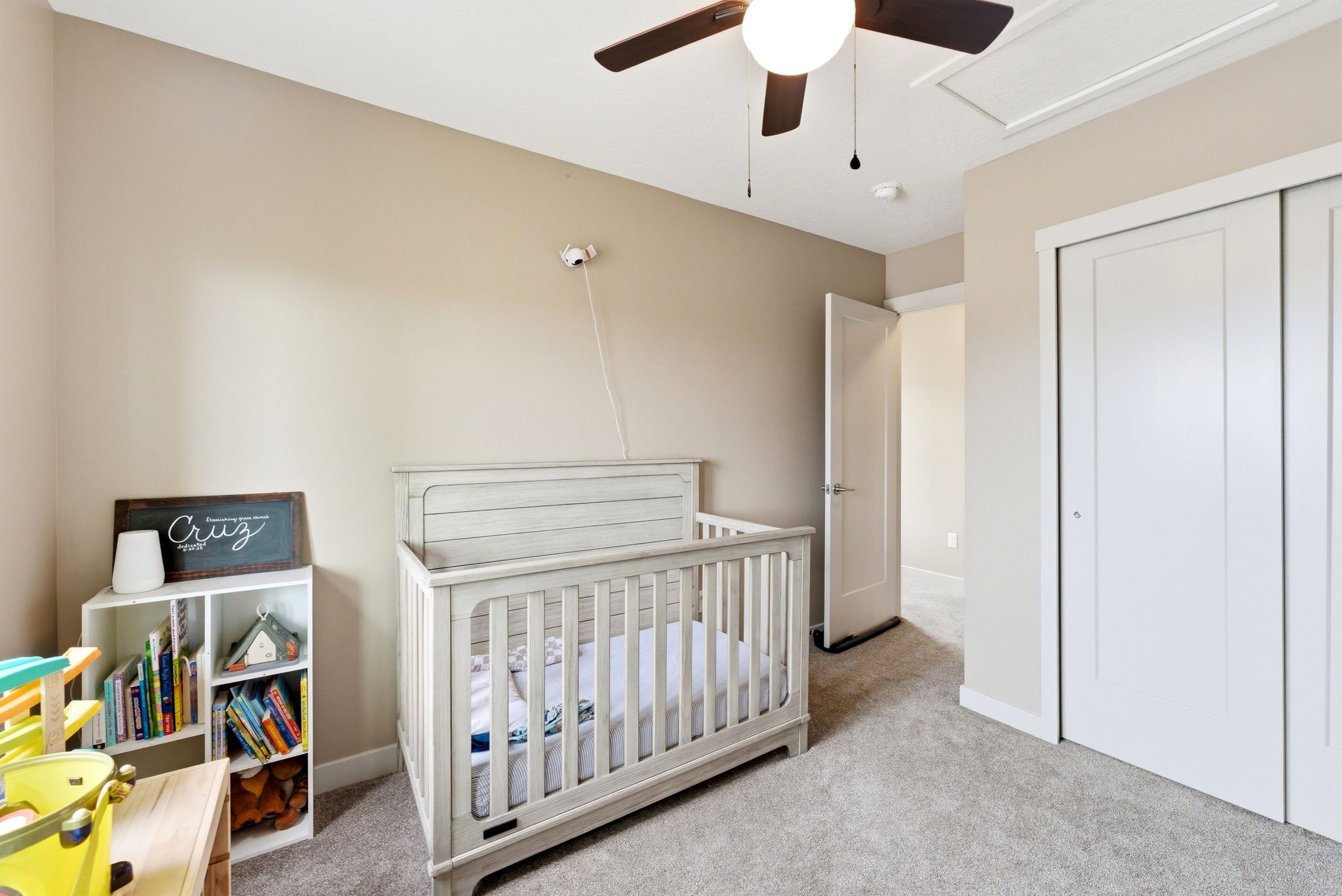 Bedroom featuring a nursery area, light colored carpet, a closet, and a ceiling fan