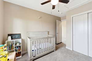Bedroom featuring a nursery area, light colored carpet, a closet, and a ceiling fan