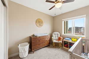 Bedroom featuring light colored carpet, a nursery area, and a ceiling fan