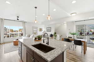 Kitchen featuring light wood-type flooring, an island with sink, open floor plan, and light stone counters