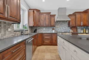 Kitchen with dark stone counters, exhaust hood, dishwasher, dual tone cabinetry, and stone finish floors