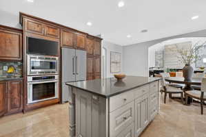 Kitchen featuring built in appliances, a kitchen island, arched walkways, recessed lighting, and tasteful backsplash