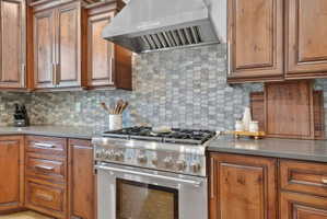 Kitchen with high end stove, wood finish cabinets, decorative backsplash, and light stone counters