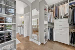 Walk in closet with light stone finish floors and arched walkways