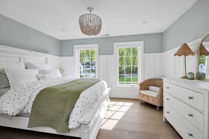 Bedroom with a decorative wall, light wood-style floors, hanging lights, and a wainscoted wall