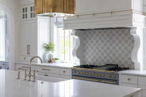 Kitchen featuring white cabinetry, light stone countertops, range with gas cooktop, glass fronted cabinets, and arched walkways