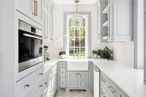 Kitchen featuring oven, gray cabinetry, light stone counters, pendant lighting, and glass insert cabinets
