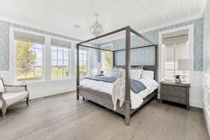 Bedroom featuring wallpapered walls, wainscoting, a decorative wall, light wood-type flooring, and suspended lighting