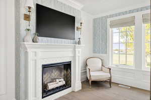 Living area featuring crown molding, wainscoting, light wood finished floors, a glass covered fireplace, and a decorative wall