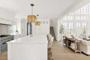 Kitchen with white cabinetry, double oven range, open floor plan, a center island with sink, and light wood finished floors