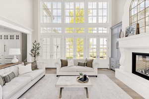 Living room featuring a glass covered fireplace, a high ceiling, french doors, and wood finished floors