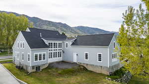 Back of house featuring a mountain view, a lawn, and roof with shingles