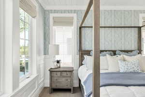 Bedroom with ornamental molding, a wainscoted wall, wallpapered walls, a decorative wall, and wood finished floors