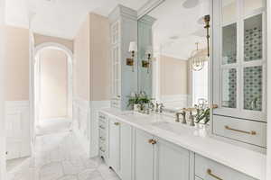Bathroom featuring double vanity, a wainscoted wall, light marble finish floors, and a decorative wall