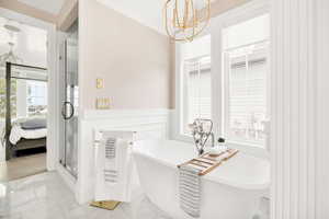 Ensuite bathroom featuring suspended lighting, a soaking tub, a stall shower, light marble finish floors, and plenty of natural light