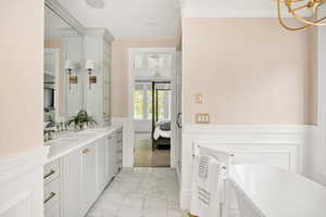 Ensuite bathroom with double vanity, a wainscoted wall, hanging lights, a soaking tub, and a decorative wall