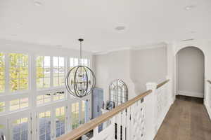 Hall with ornamental molding, hanging lights, hardwood / wood-style flooring, and an upstairs landing