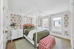 Bedroom with wood-type flooring, ornamental molding, and wallpapered walls