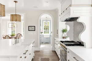 Kitchen featuring white cabinets, light stone counters, dark wood-style flooring, and range with gas cooktop