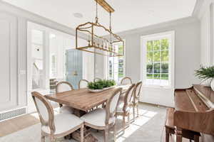 Dining space featuring suspended lighting, crown molding, plenty of natural light, light wood-type flooring, and a decorative wall