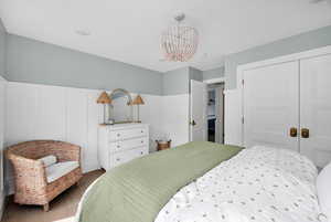 Bedroom featuring a decorative wall, hanging lights, a closet, a wainscoted wall, and wood finished floors
