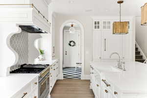Kitchen featuring arched walkways, glass insert cabinets, range with two ovens, and light stone countertops