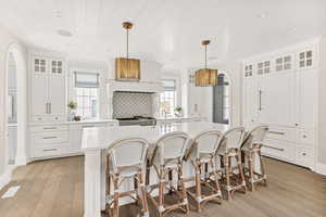 Kitchen featuring glass fronted cabinets, arched walkways, hanging light fixtures, an island with sink, and light wood-style floors