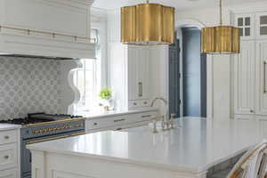 Kitchen with white cabinetry, gas range, light stone counters, and glass fronted cabinets