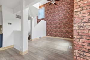 Unfurnished living room with a high ceiling, brick wall, light wood finished floors, and a ceiling fan