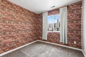 Unfurnished room featuring brick wall and carpet flooring
