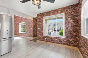 Unfurnished living room featuring brick wall, light wood-style flooring, and ceiling fan