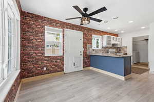Kitchen with a ceiling fan, brick wall, a peninsula, glass fronted cabinets, and light wood finished floors