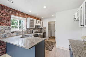 Kitchen featuring glass fronted cabinets, a peninsula, light wood-style floors, recessed lighting, and white gas stove