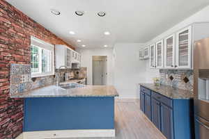 Kitchen featuring glass fronted cabinets, tasteful backsplash, stainless steel refrigerator with ice dispenser, a peninsula, and recessed lighting