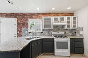 Two tone kitchen with white gas stove, glass fronted cabinets, two tone color scheme, tasteful backsplash, and light stone counters