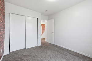 Unfurnished bedroom featuring carpet, a closet, and brick wall