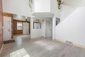 Unfurnished living room featuring brick wall, a high ceiling, light wood finished floors, and a ceiling fan