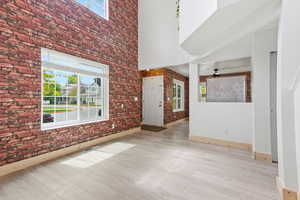 Foyer featuring brick wall, plenty of natural light, a high ceiling, light wood-style floors, and ceiling fan