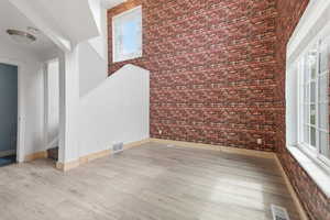 Unfurnished room featuring brick wall, a high ceiling, and light wood-style flooring