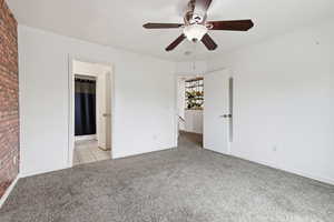 Unfurnished bedroom with light colored carpet, ceiling fan, and brick wall