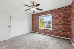Unfurnished room with brick wall, ceiling fan, and light carpet