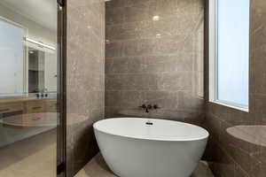 Full bath featuring tile walls, a freestanding bath, and vanity