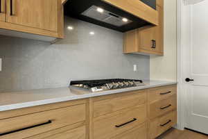 Kitchen with light stone countertops, stainless steel gas stovetop, tasteful backsplash, and wood finished floors