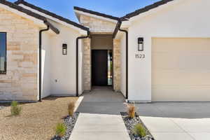 Property entrance with stone siding, stucco siding, concrete driveway, and a garage
