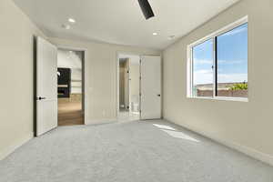 Unfurnished bedroom with connected bathroom, light colored carpet, a lit fireplace, recessed lighting, and ceiling fan