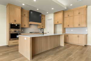 Kitchen with stainless steel appliances, backsplash, an island with sink, light wood-style flooring, and light wood finish cabinets