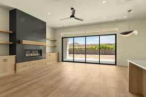 Unfurnished living room with a mountain view, recessed lighting, a ceiling fan, a glass covered fireplace, and light wood-style flooring