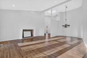 Unfurnished living room featuring a fireplace with raised hearth, a chandelier, dark wood-style flooring, ceiling fan, and lofted ceiling