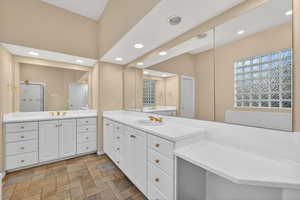 Bathroom featuring two vanities, light stone finish flooring, and recessed lighting